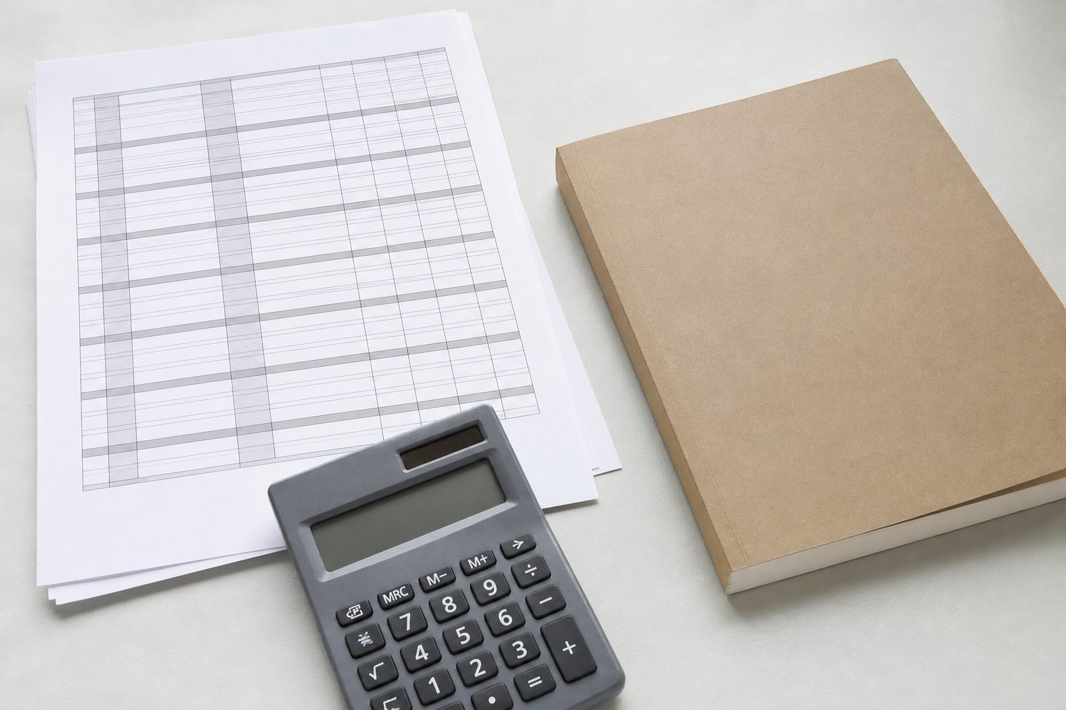 A printed spreadsheet page, calculator and proof paperback arranged on a bright pale desk